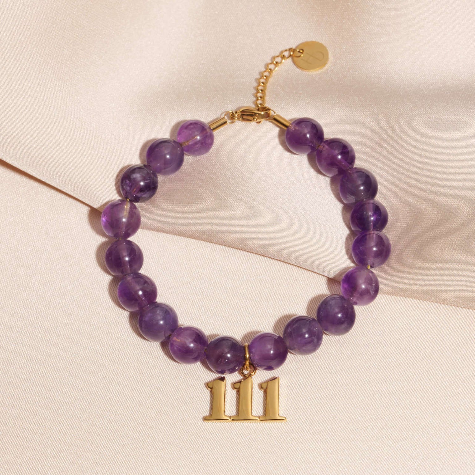 111 gold charm on beaded amethyst bracelet laying on silk