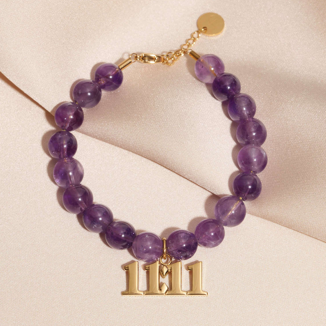 11:11 gold charm on beaded amethyst bracelet laying on silk