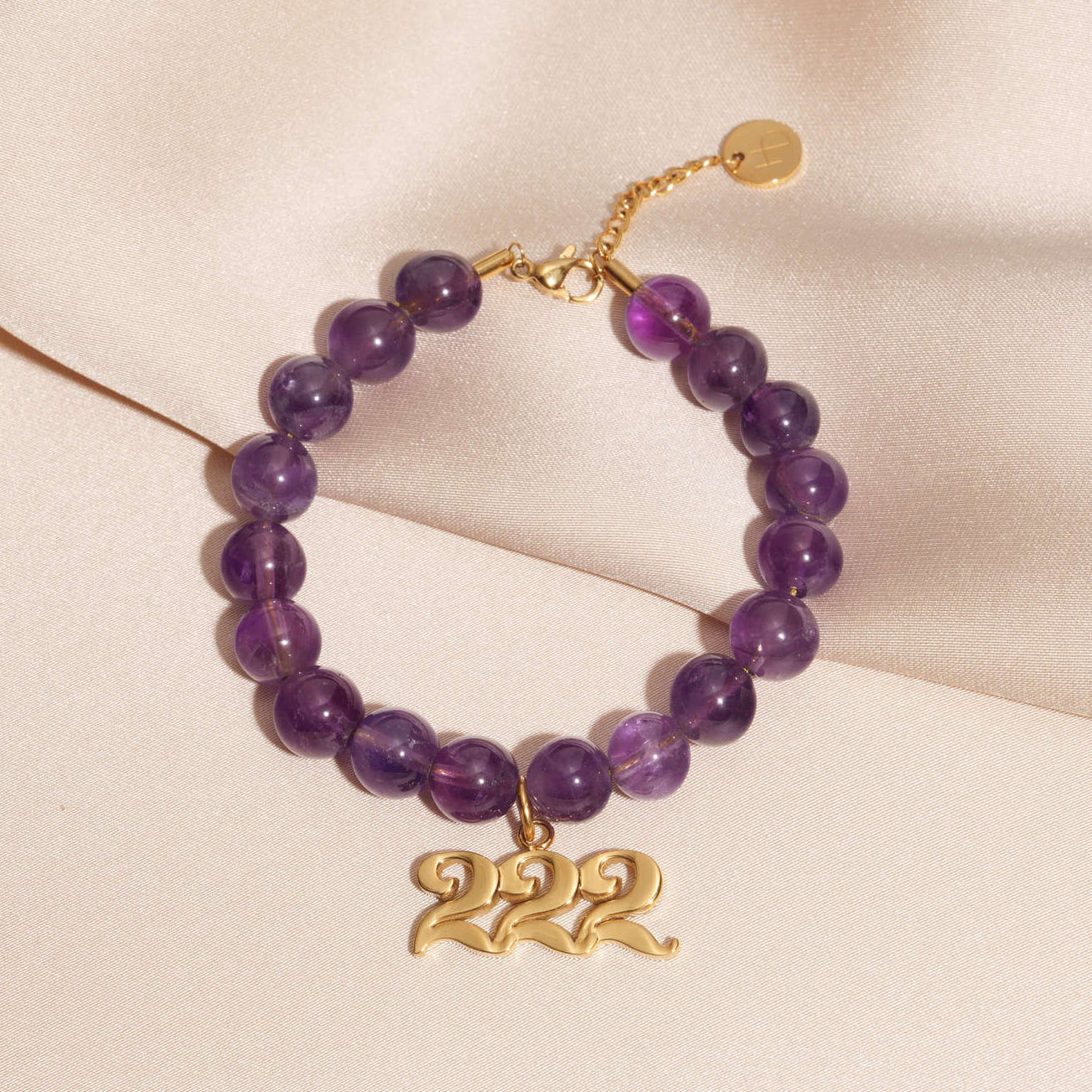 222 gold charm on beaded amethyst bracelet laying on silk