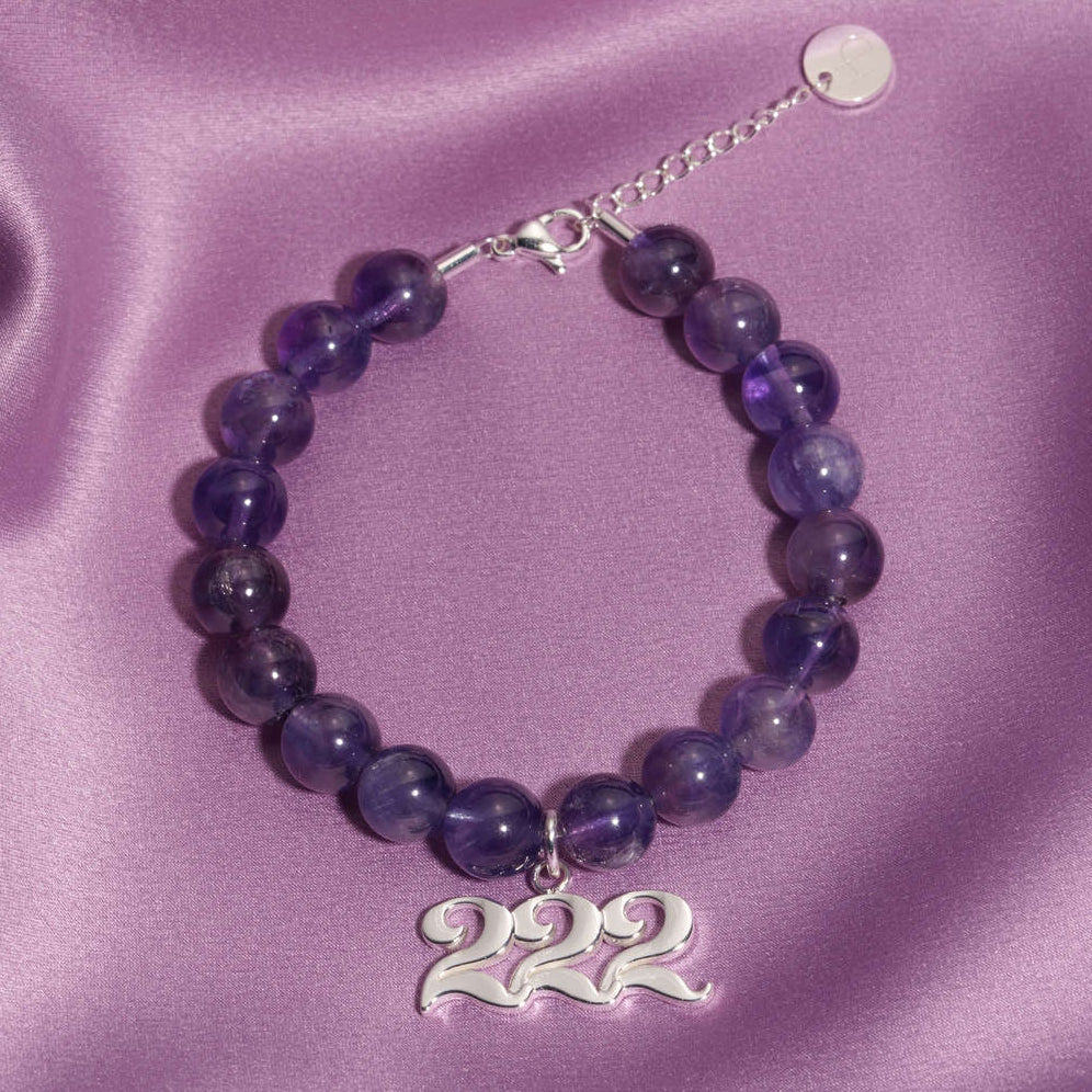 222 silver charm on beaded amethyst bracelet laying on silk