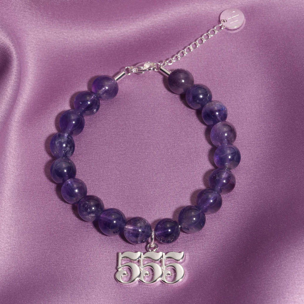 555 Silver charm on beaded amethyst bracelet laying on silk