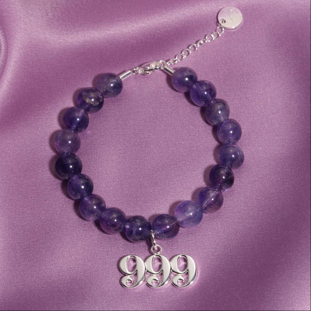 999 Silver charm on beaded amethyst bracelet laying on silk