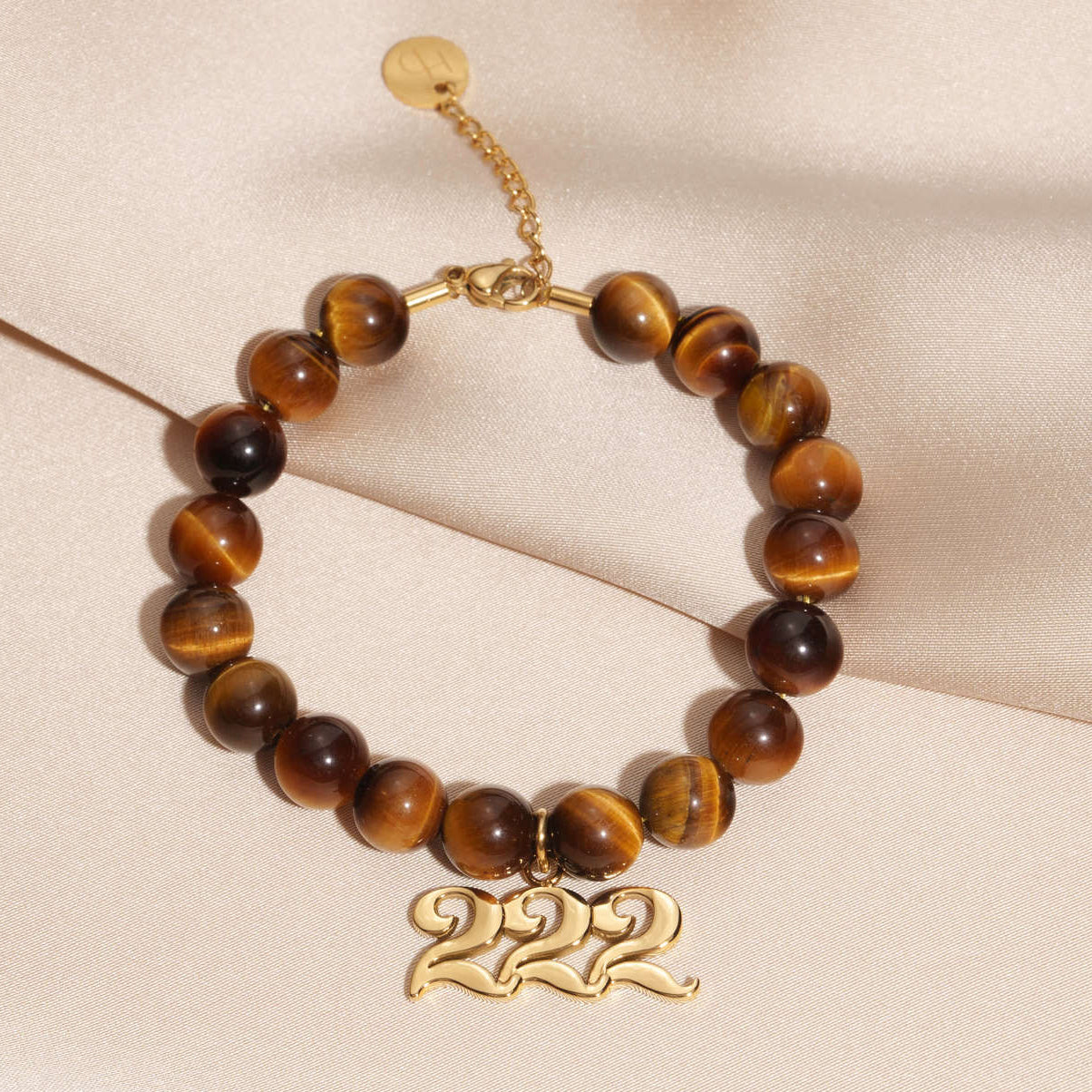 222 Gold charm on beaded Tigers Eye bracelet laying on silk
