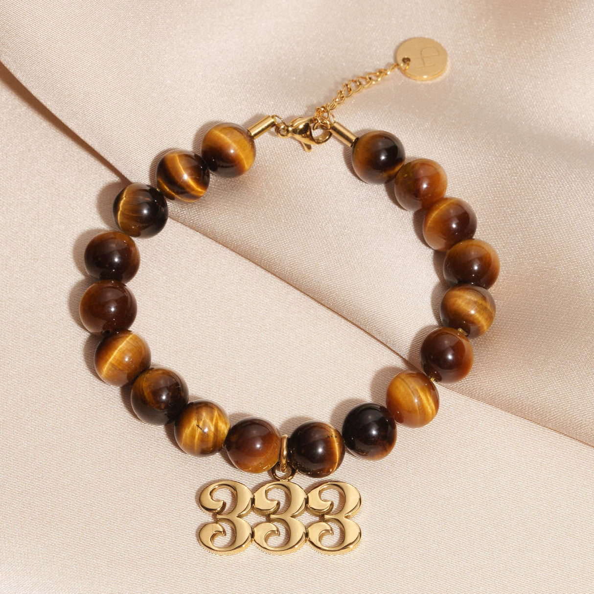 333 Gold charm on beaded Tigers Eye bracelet laying on silk
