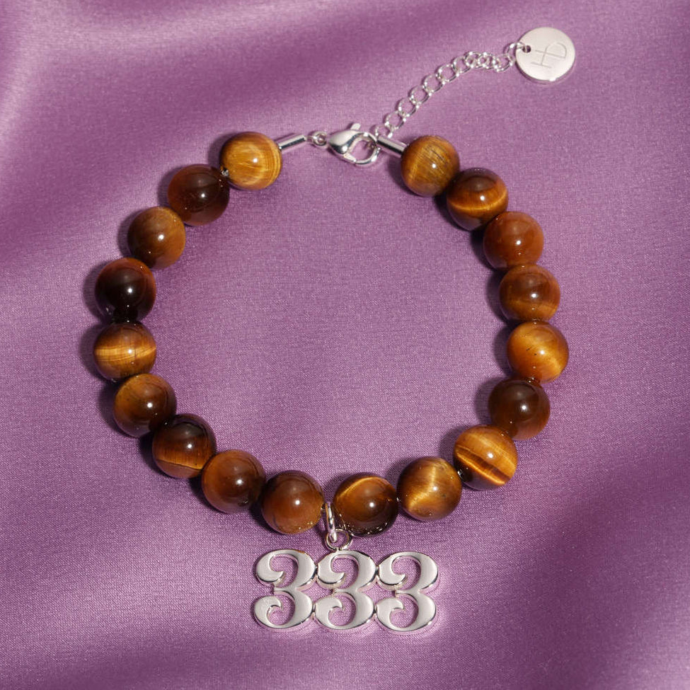 333 Silver charm on beaded Tigers Eye bracelet laying on silk
