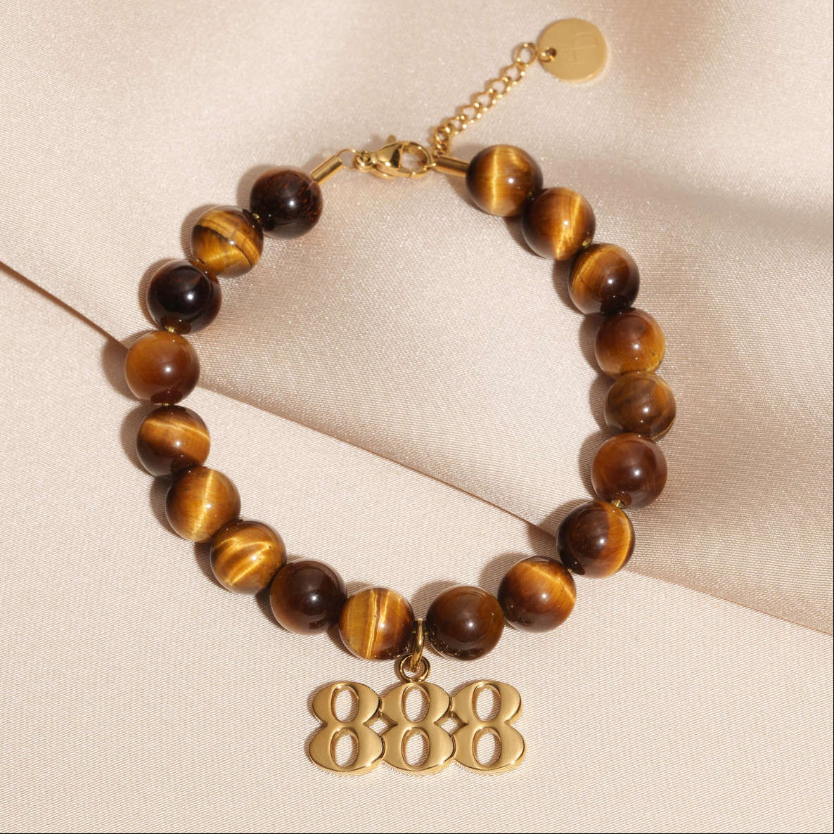 888 Gold charm on beaded Tigers Eye bracelet laying on silk
