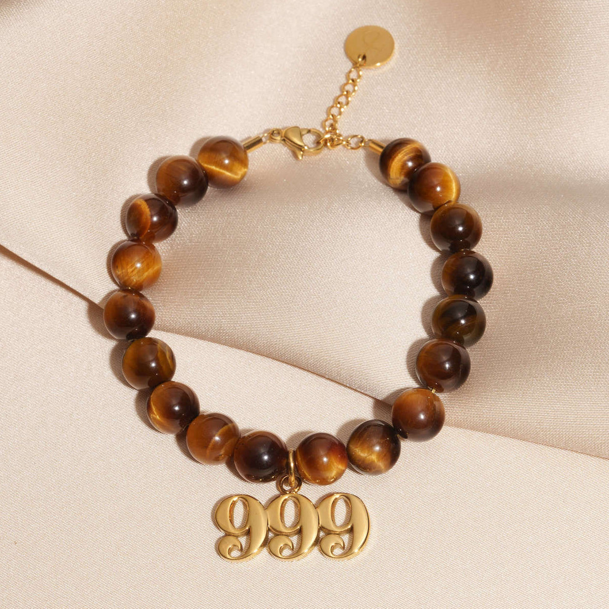 999 Gold charm on beaded Tigers Eye bracelet laying on silk
