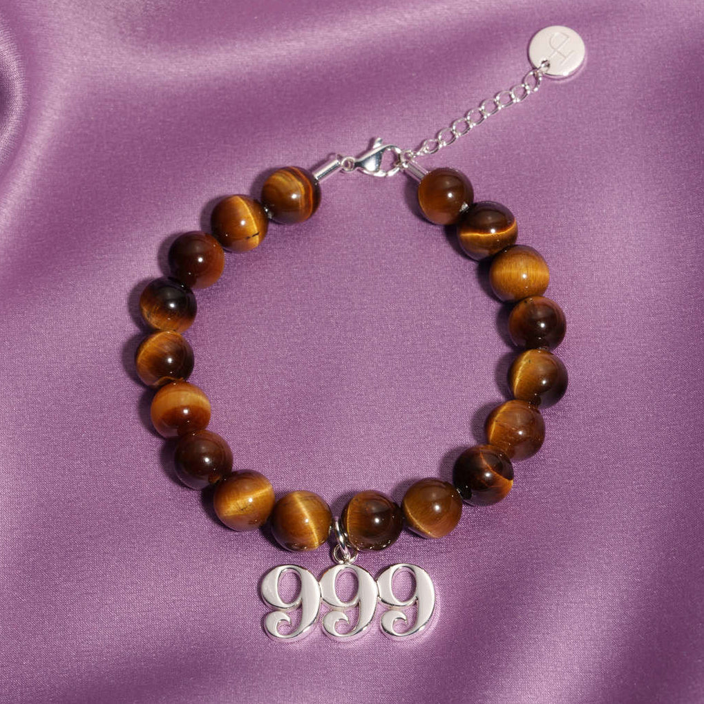 999 Silver charm on beaded Tigers Eye bracelet laying on silk
