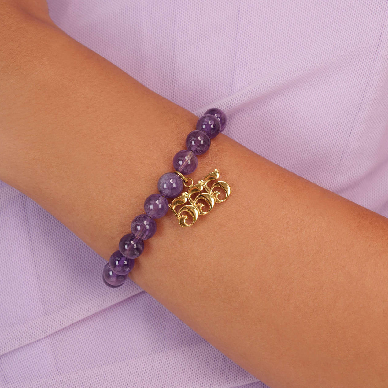 High quality purple amethyst beads with dangling 555 gold charm on wrist

