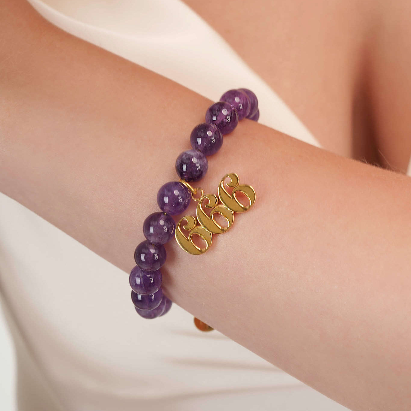 High quality purple amethyst beads with dangling 666 gold charm on wrist
